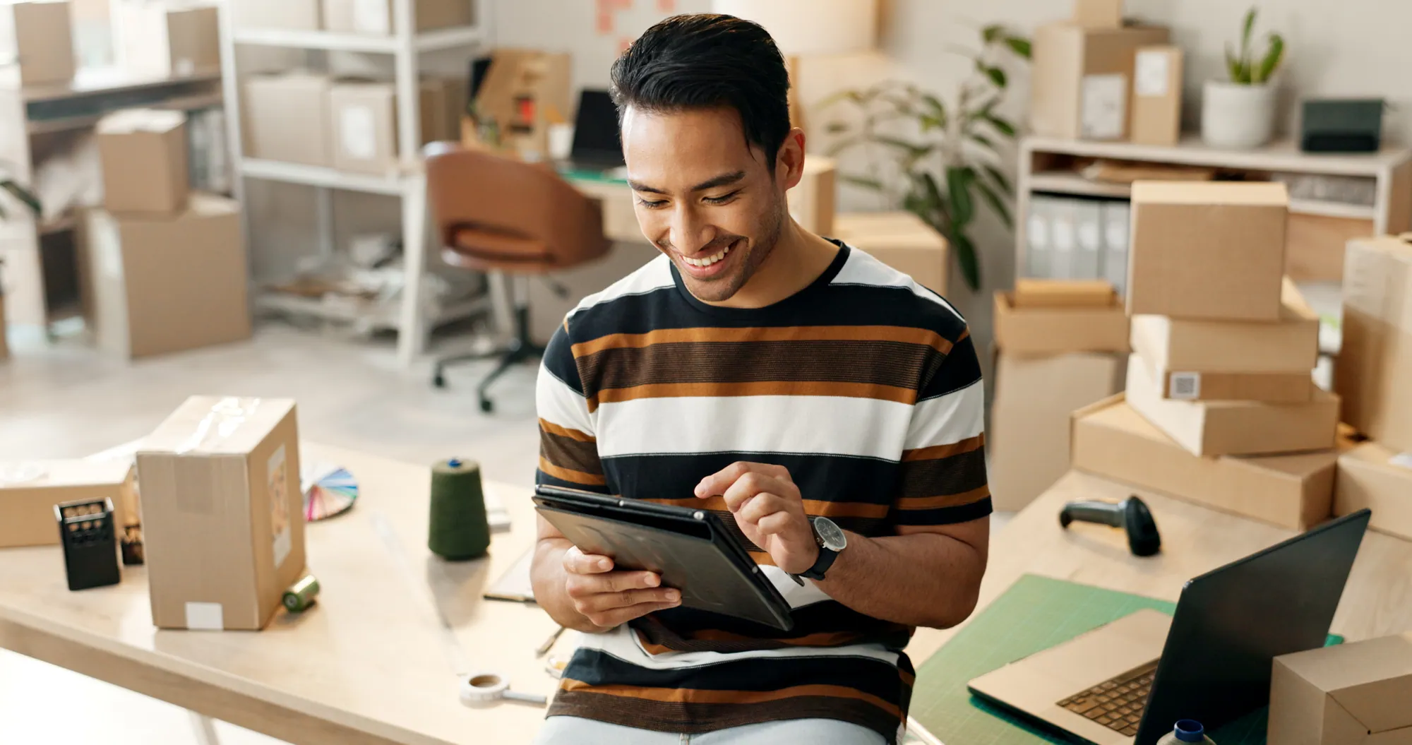 Business owner reviewing orders on a tablet among packed goods